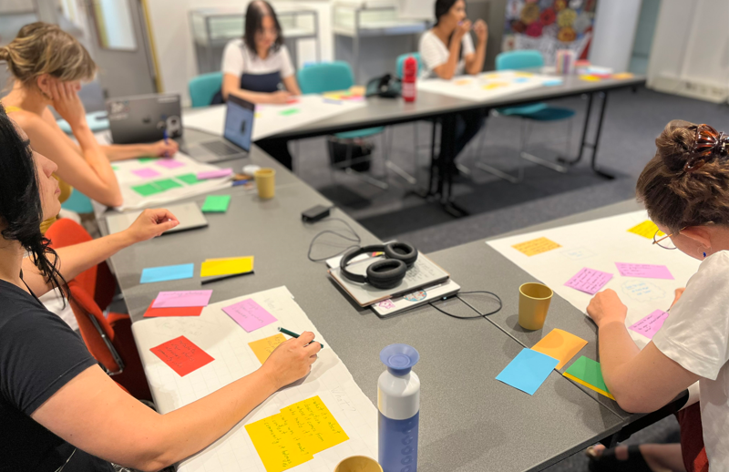 Participants writing their ideas on colorful post-its on tables at the CLARIAH Summer School in the IISG building