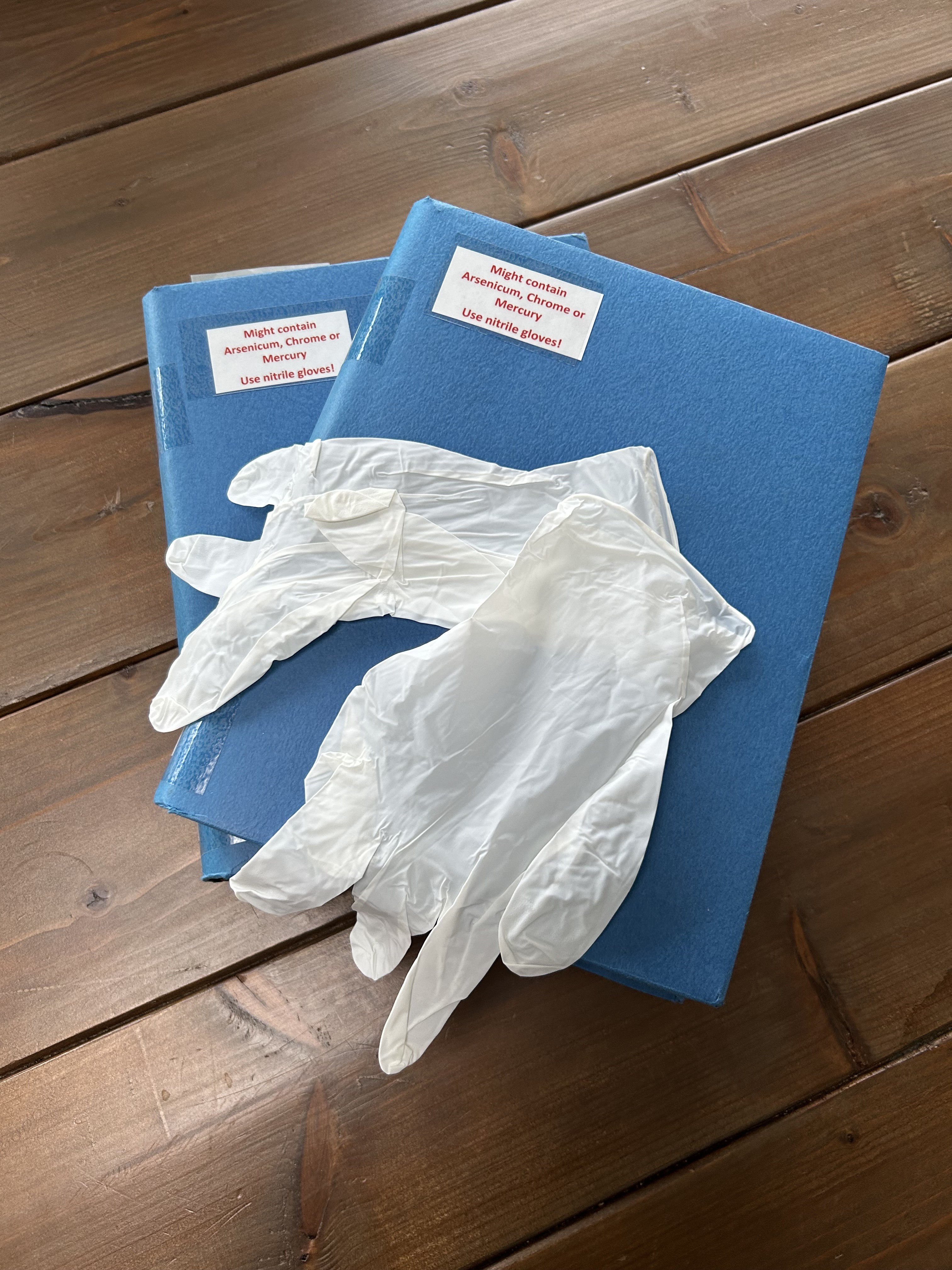 Afbeelding van reisverslagen, met de tekst 'Kan arseen, chroom of kwik bevatten'. Er zit een blauwe kaft omheen en er liggen rubberen handschoenen op. 