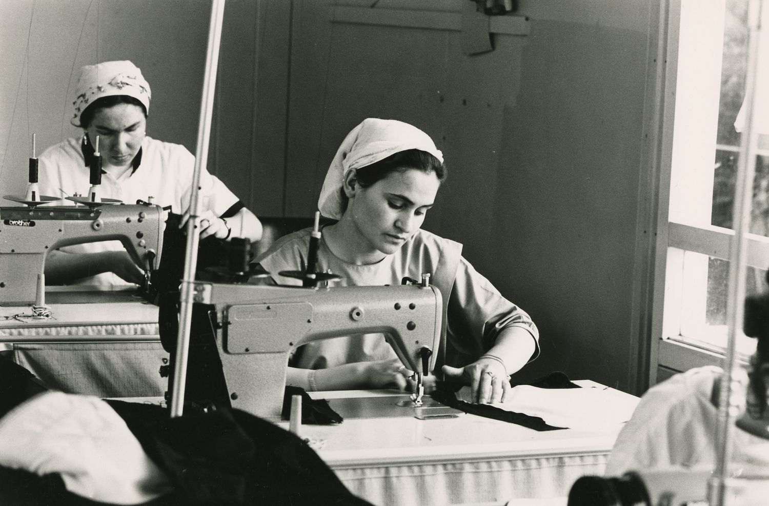This is a black-and-white photograph taken by Maya Pejić in 1986 of two Turkish women sitting at a sewing machine in a textile factory.