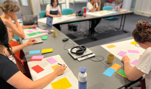 Participants writing their ideas on colorful post-its on tables at the CLARIAH Summer School in the IISG building