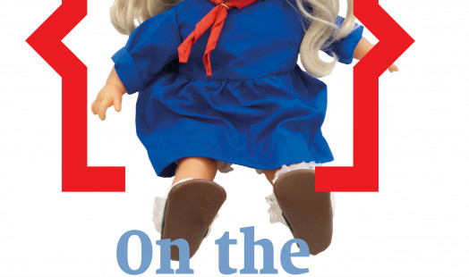 Cover of On the Waterfront 36. Photograph of a doll based on the cartoon character Mieke Meijer, designed by Ger Sligte. The doll depicts a little girl in a blue dress with red bows in her long blonde hair.
